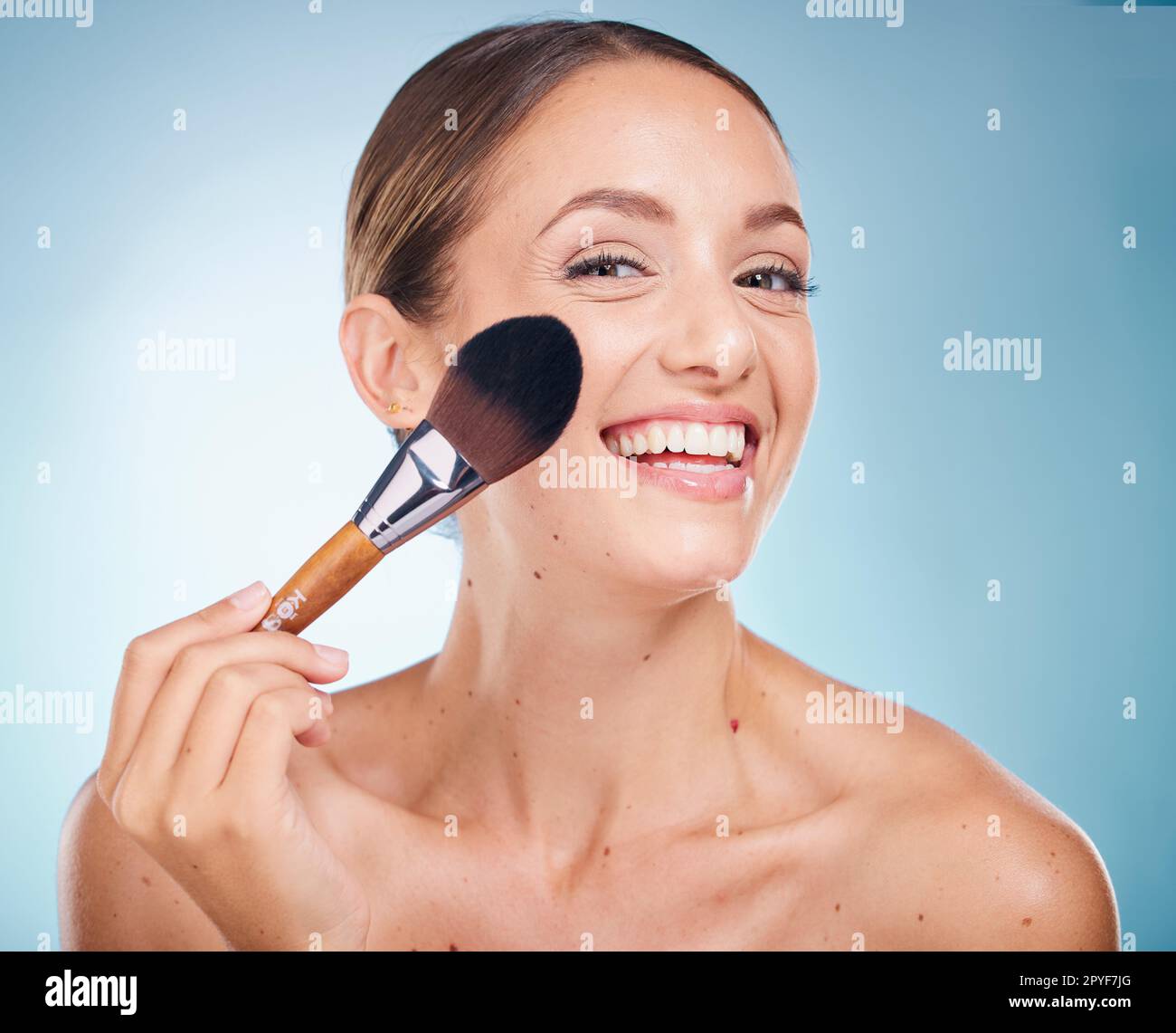 Gesichtsbild, Hautpflege und Frau mit Make-up-Bürste im Studio isoliert auf blauem Hintergrund. Produkt, Kosmetikwerkzeug und Ästhetik eines glücklichen weiblichen Modells mit Accessoire, um die Grundlage für Schönheit zu schaffen Stockfoto