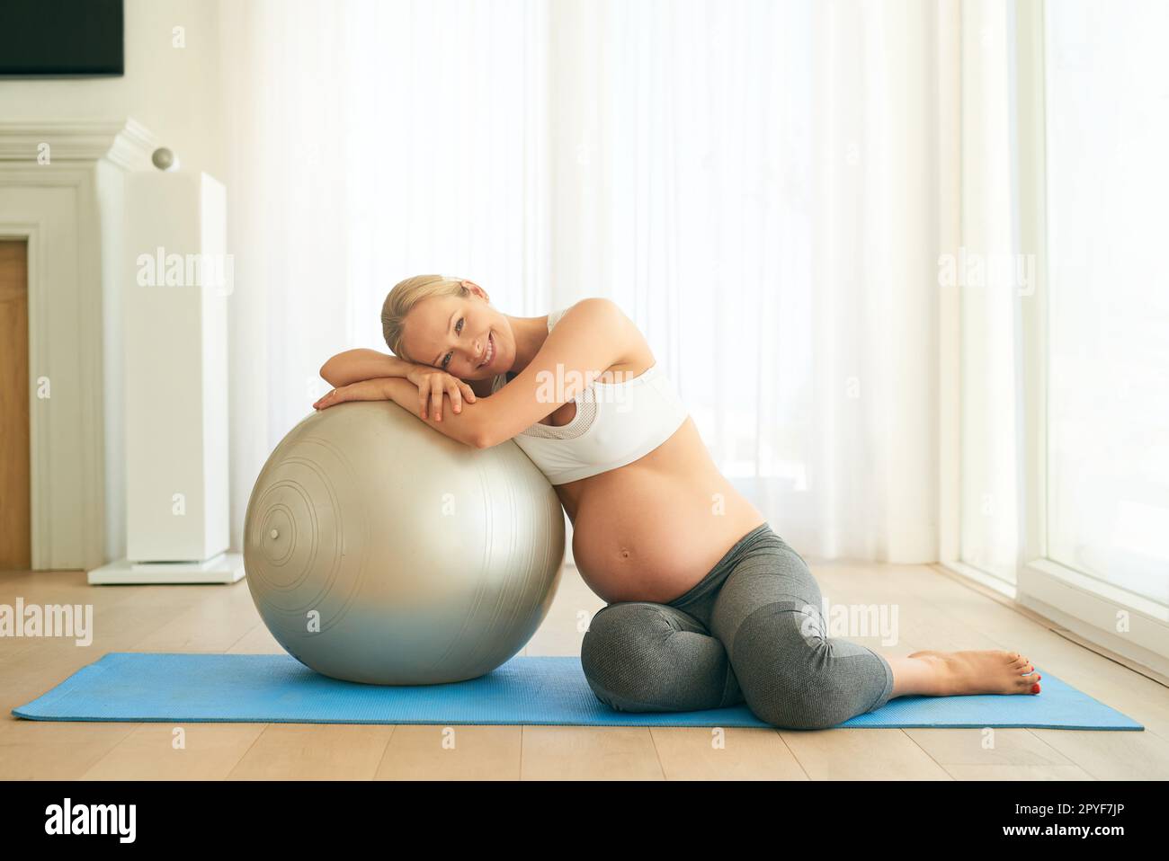 Gesund zu bleiben für mich und für Mini-mich. Eine schwangere Frau, die zu Hause mit einem Sportball trainiert. Stockfoto