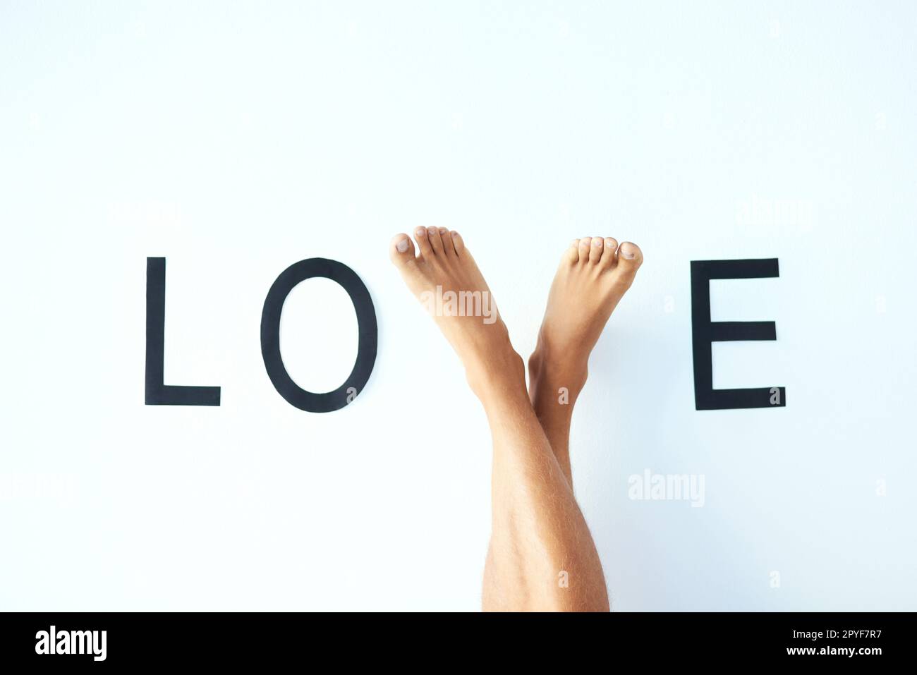 Ich werde gehen, bis ich eines Tages Liebe finde. Studiofoto eines unbekannten mannes kreuzte die Beine mit den Füßen und formte den Buchstaben V im Wort LIEBE. Stockfoto