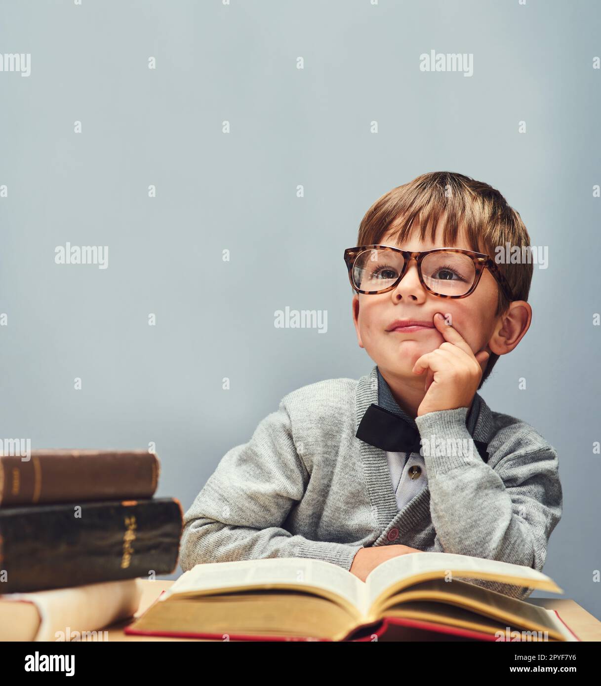 Die Zukunft gehört den Neugierigen. Studioaufnahme eines kleinen Jungen, der Bücher liest und vor grauem Hintergrund nachdenklich aussieht. Stockfoto