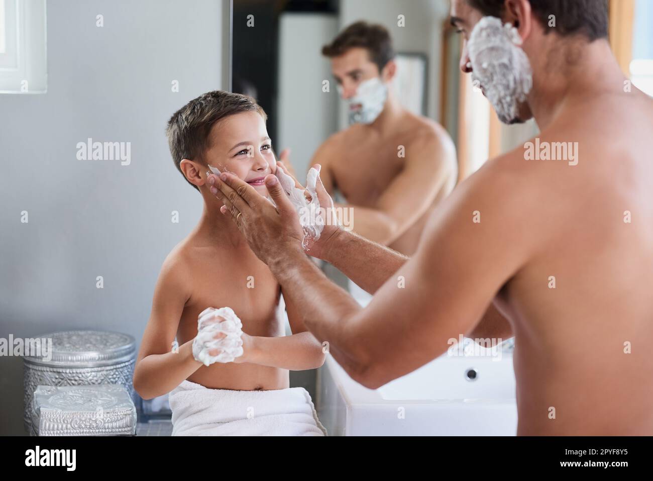 So macht man das. Ein gutaussehender junger Mann, der seinem Sohn beibringt, wie man sich im Bad rasiert. Stockfoto