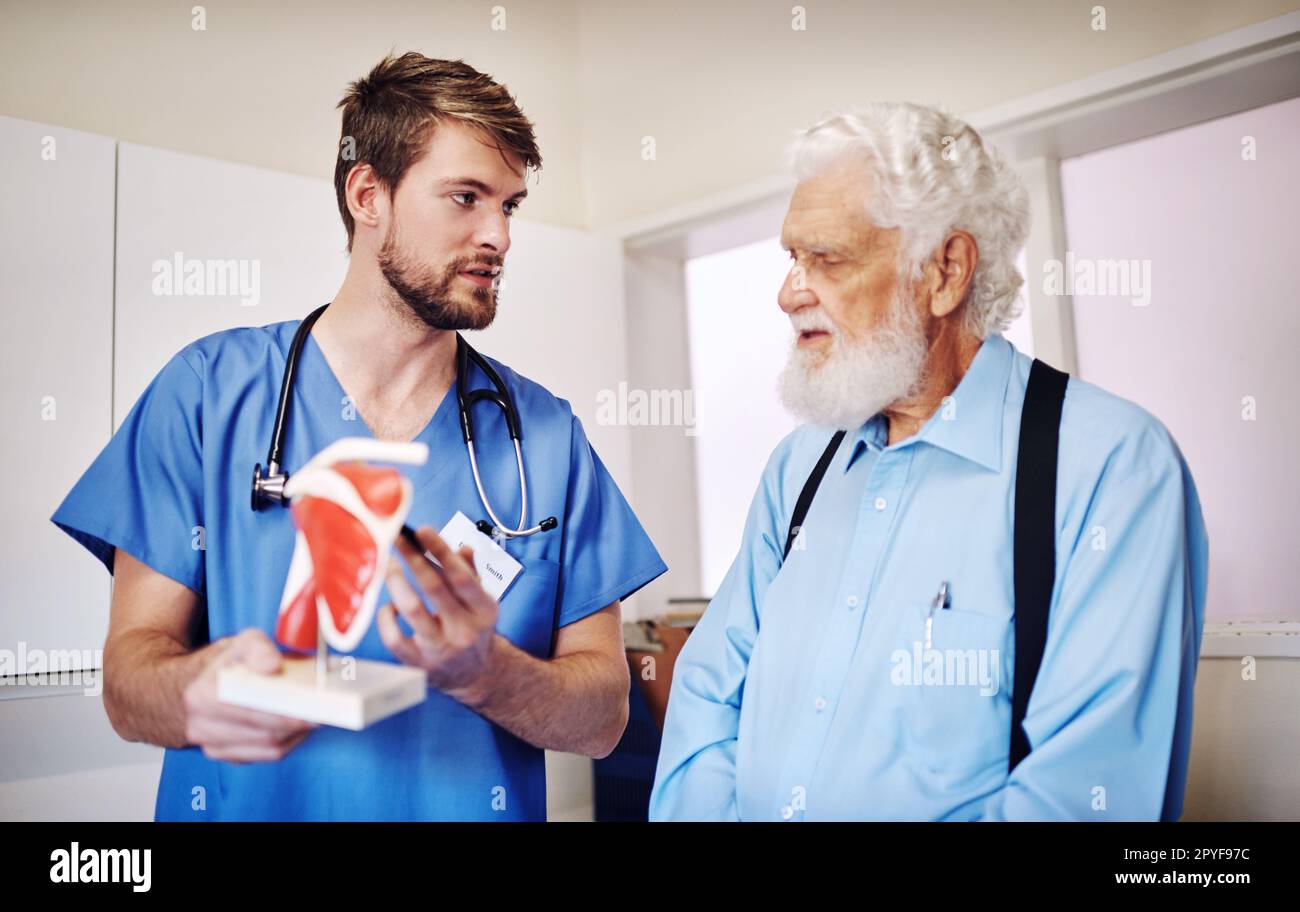 Ich gebe nur einem älteren Patienten ein praktisches Beispiel. Ein junger Arzt, der ein Modell benutzt, um seinem älteren Patienten eine Diagnose zu erklären. Stockfoto