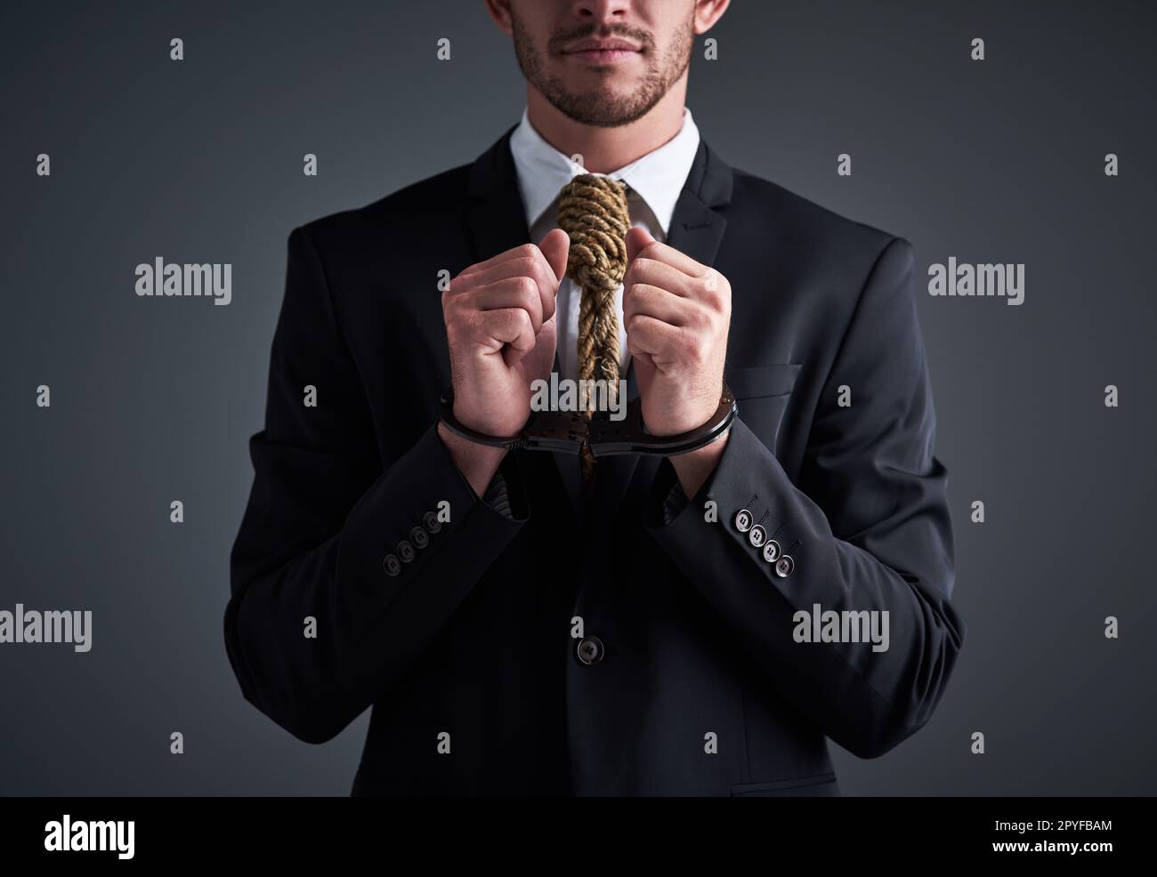 Unternehmensverbrecher. Studiofoto eines Geschäftsmannes mit Handschellen und einer Schlinge um den Hals, die für eine Krawatte vor grauem Hintergrund gefesselt ist. Stockfoto