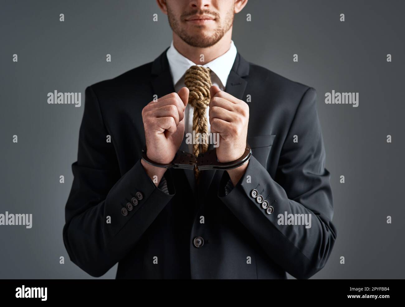 Unternehmensverbrecher. Studiofoto eines Geschäftsmannes mit Handschellen und einer Schlinge um den Hals, die für eine Krawatte vor grauem Hintergrund gefesselt ist. Stockfoto