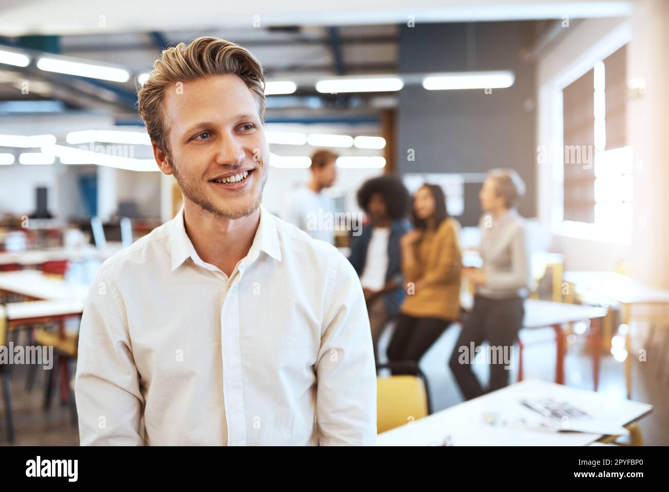 Denken Sie an einen Masterplan. Ein hübscher junger Geschäftsmann im Büro mit seinen Kollegen im Hintergrund. Stockfoto