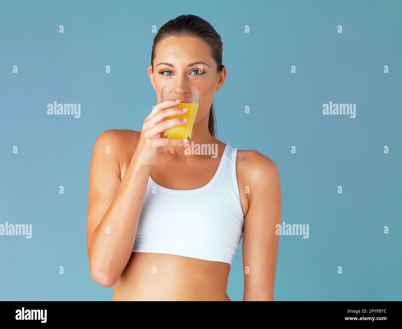 Manche nennen es Orangensaft, ich nenne es flüssiges Gold. Studiofoto einer fitten jungen Frau, die ein Glas Saft trinkt, vor blauem Hintergrund. Stockfoto