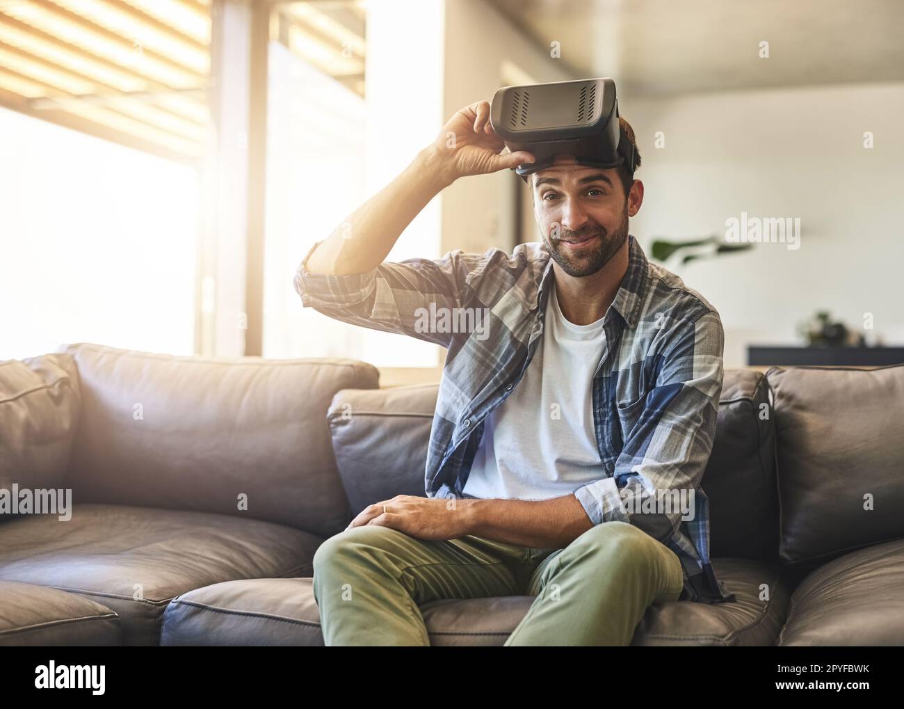 Ich bin dabei, eine andere Welt zu betreten. Ein junger Mann, der zu Hause ein Virtual-Reality-Headset auf dem Sofa verwendet. Stockfoto
