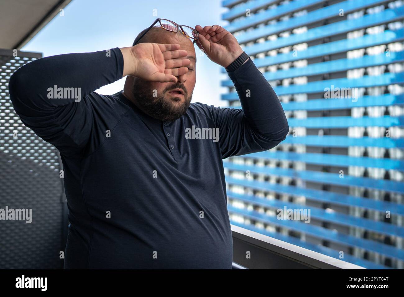 Übergewichtiger Mann, Kopfschmerzen, Augen reiben, im Sommer auf dem Balkon stehen. Stockfoto