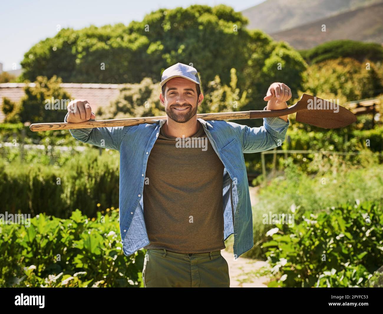 Das Leben auf einer Farm ist einfach besser. Porträt eines glücklichen jungen Bauern, der auf den Feldern seines Bauernhofs mit einem Spaten posiert. Stockfoto