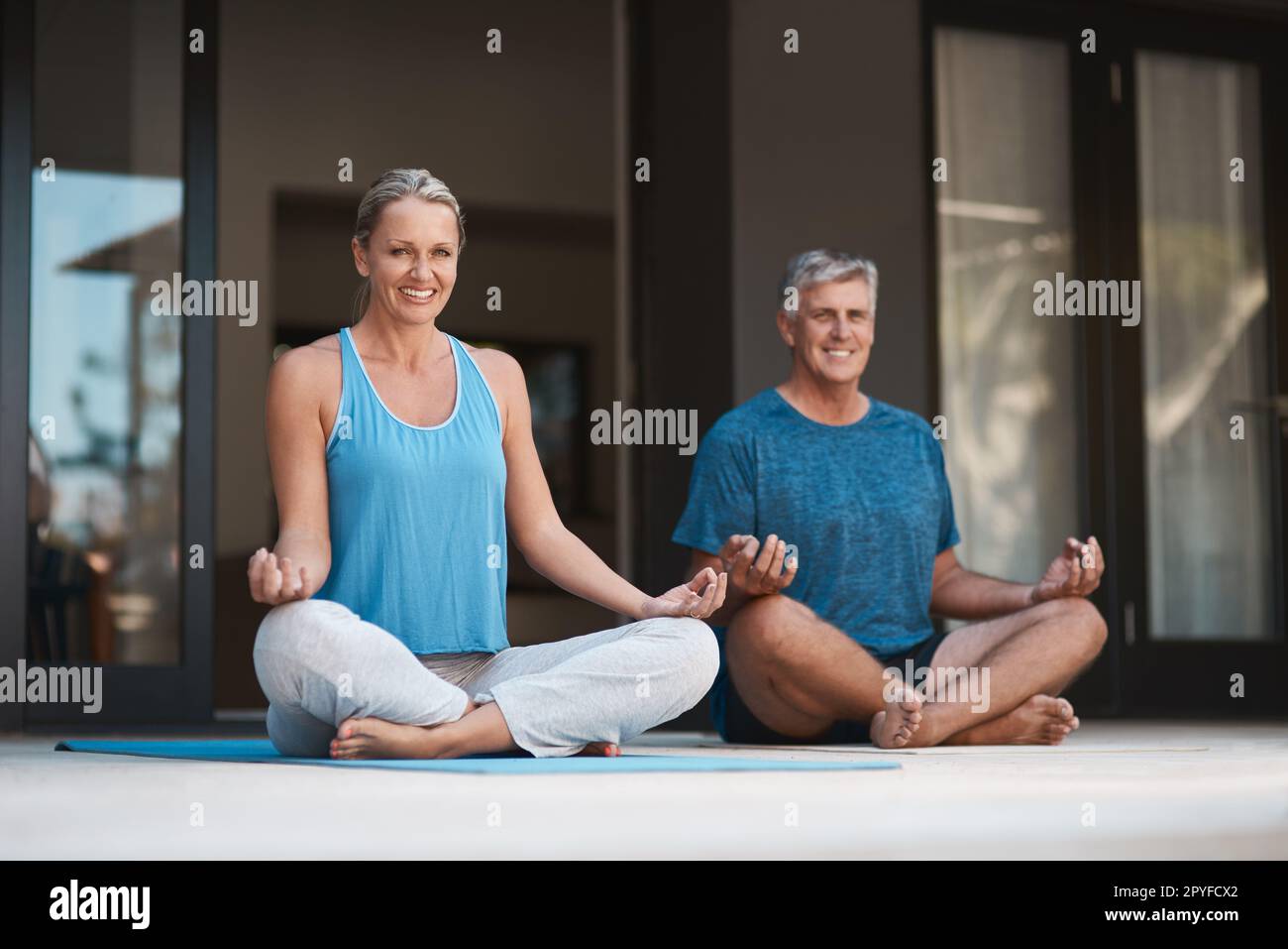 Yoga bringt ein Lächeln ins Gesicht und in den Geist. Reifes und glückliches Paar, das sich in einer Yoga-Pose mit überkreuzten Beinen aufführt. Stockfoto