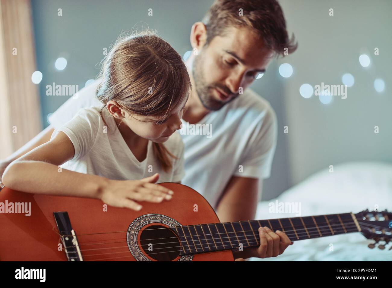 Zusammen wunderschöne Musik machen. Ein kleines Mädchen, das mit ihrem Vater Gitarre spielt. Stockfoto