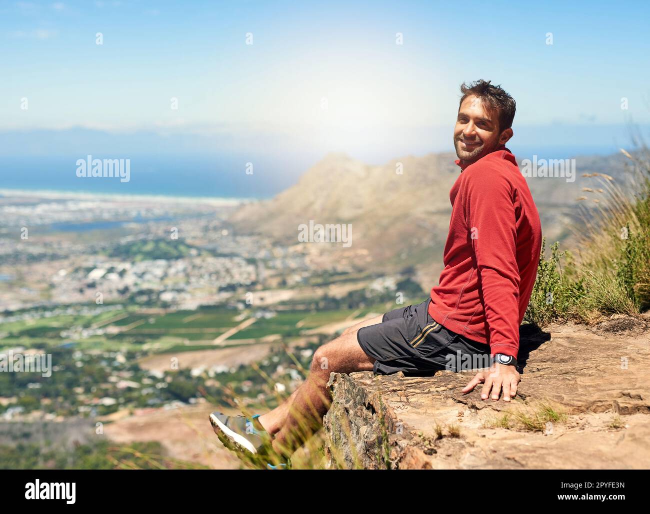 Der Aufstieg war hart, aber die Aussicht lohnt sich. Porträt eines sportlichen jungen Mannes, der die Aussicht vom Gipfel eines Berges bewundert. Stockfoto