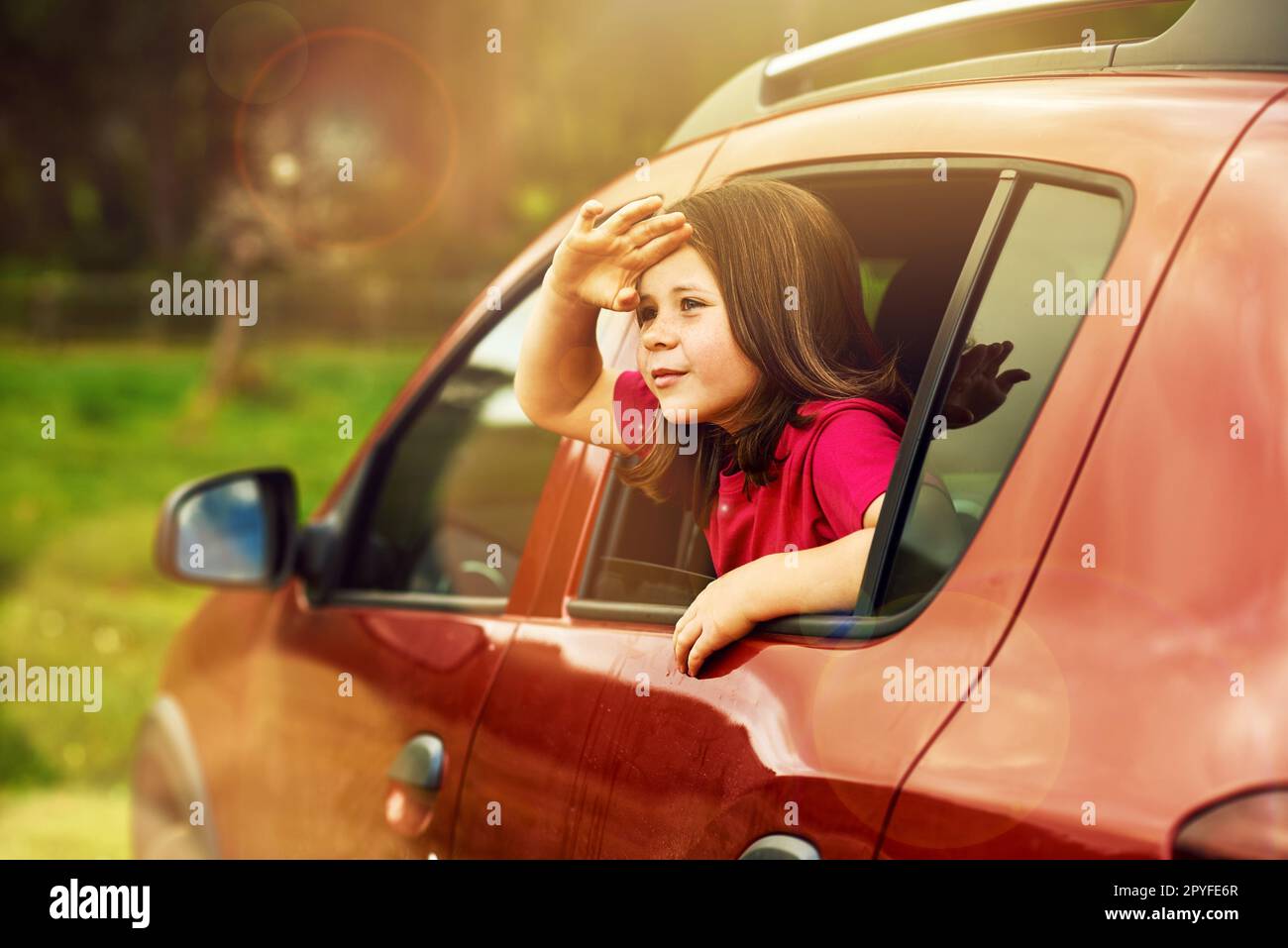 Es gibt eine ganze weite Welt zu sehen. Ein bezauberndes kleines Mädchen, das sich aus einem Autofenster lehnt. Stockfoto