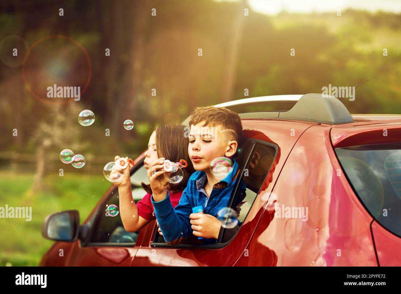 Er taumelt vor Spaß über. Zwei glückliche Kinder blasen Blasen, während sie sich zusammen aus einem Autofenster lehnten. Stockfoto