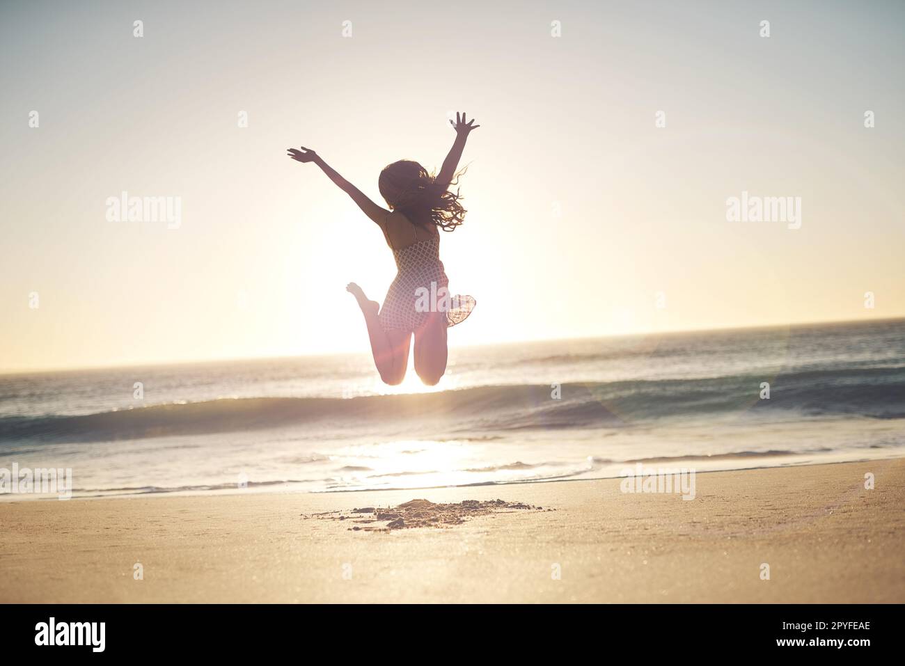 Finden Sie, was Ihnen Freude bereitet, und gehen Sie dorthin. Eine junge Frau, die am Strand in die Luft springt. Stockfoto