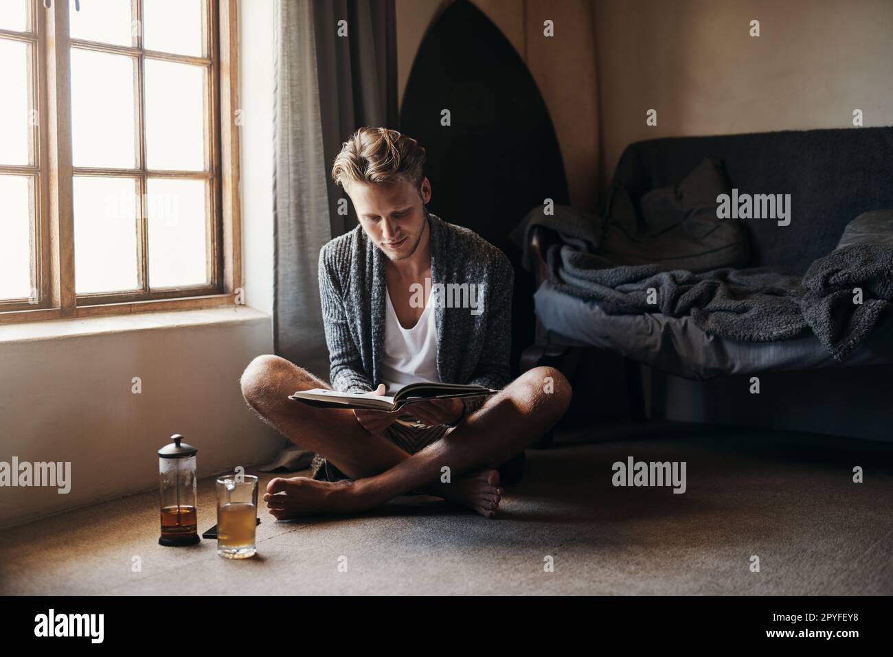 Es gibt nichts entspannenderes als eine gute Lektüre. Ein junger Mann liest ein Buch, während er zu Hause auf dem Boden sitzt. Stockfoto