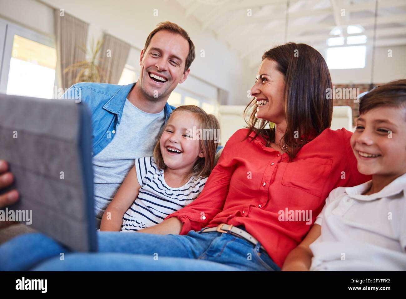 Digitale Unterhaltung für die ganze Familie. Lächelnde Eltern, die mit ihrem Sohn und ihrer Tochter zu Hause auf dem Sofa im Wohnzimmer sitzen und ein digitales Tablet benutzen. Stockfoto