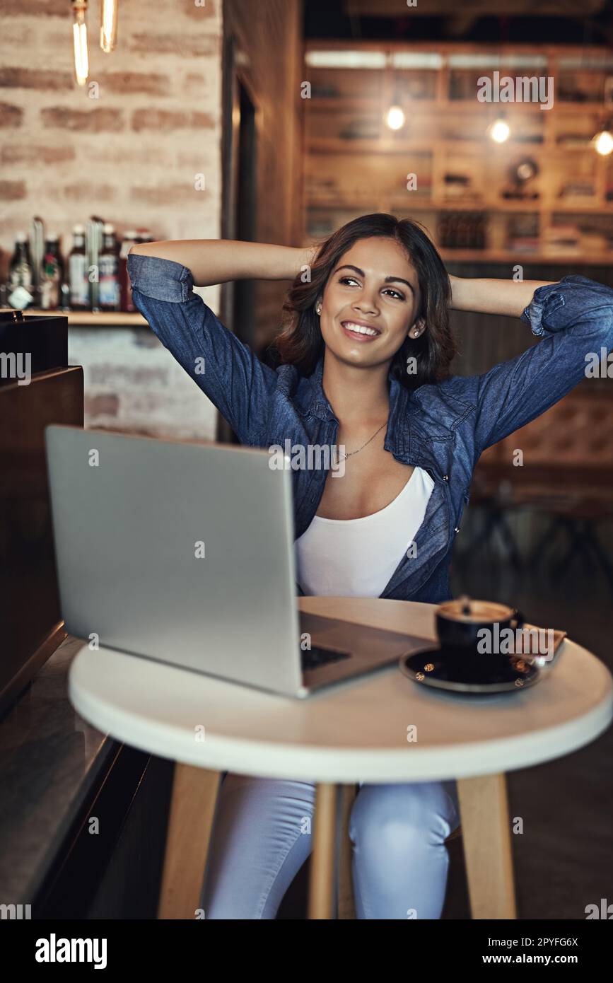Das Leben ist so viel einfacher, wenn man einfach chillt. Eine entspannte junge Frau, die ihren Laptop in einem Café benutzt. Stockfoto