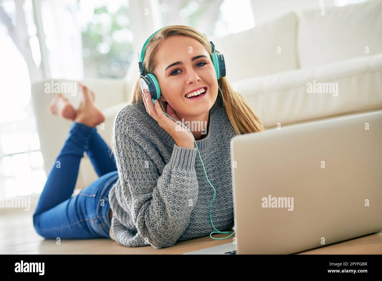 Musik am Wochenende. Eine attraktive junge Frau, die zuhause Musik auf ihrem Laptop hört. Stockfoto