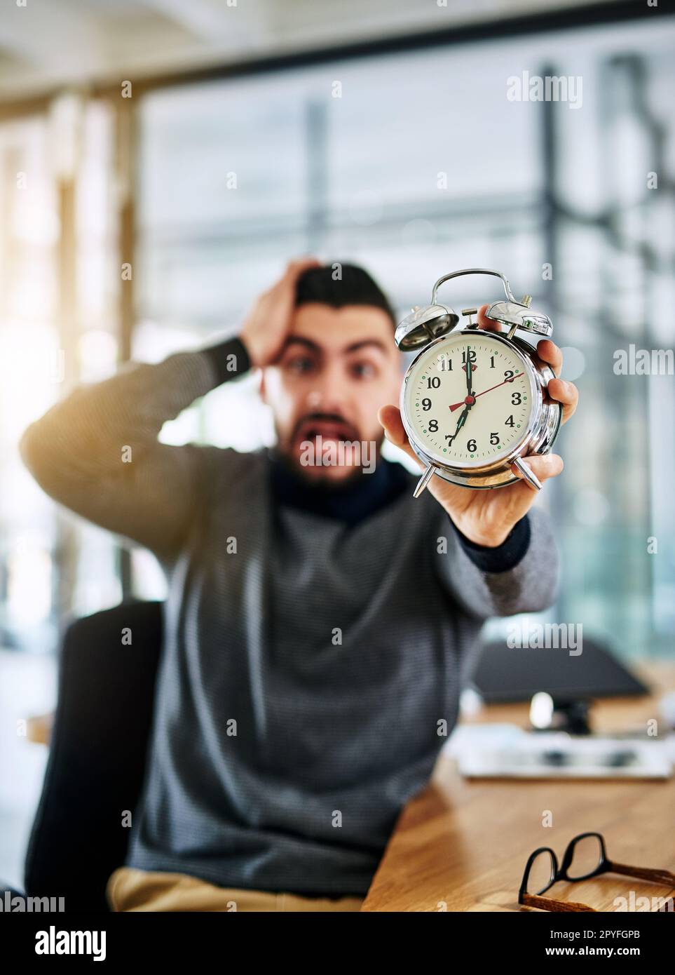 Ist es schon so weit? Porträt eines jungen Designers mit Wecker und gestresstem Blick während der Arbeit im Büro. Stockfoto