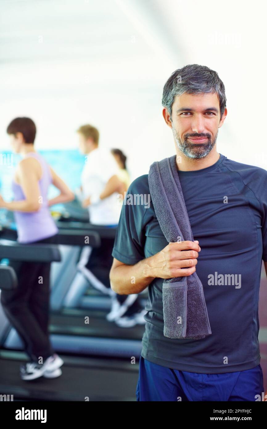 Ein Mann, der im Fitnessstudio trainiert. Porträt eines Mannes mittleren Alters, der ein Handtuch hält, während sich im Hintergrund sportlich betätigen. Stockfoto
