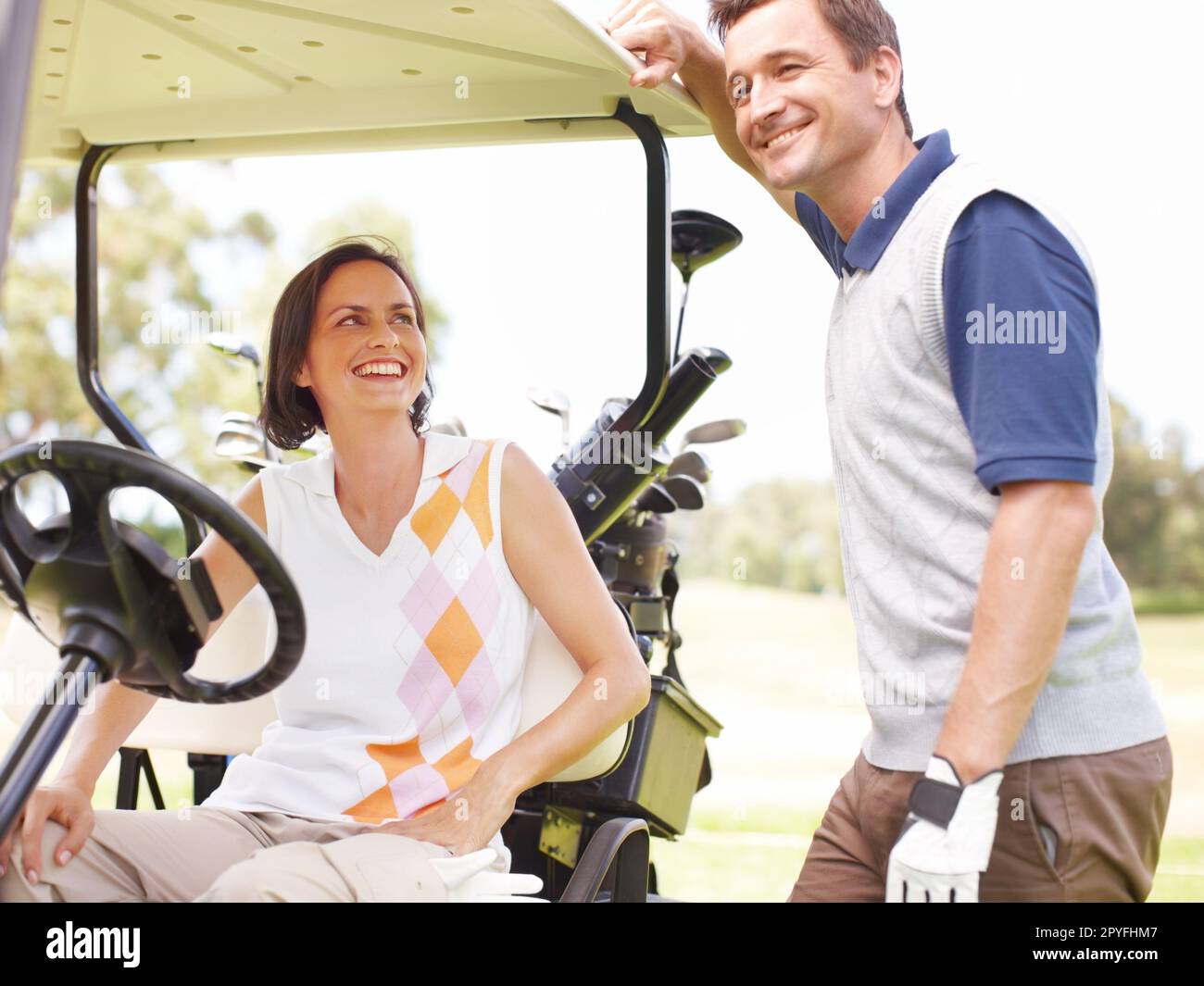 Er hat diese Runde Golf gewonnen... lächelnde Frau, die in einem Golfwagen saß und ihren Mann neben ihr stand. Stockfoto