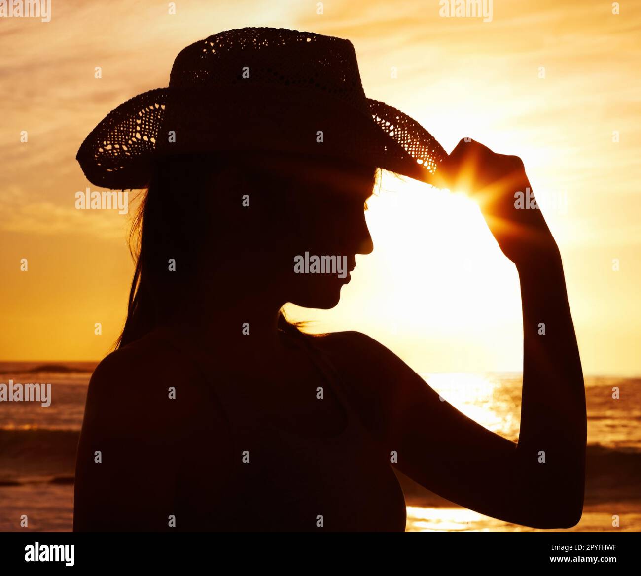 Nahaufnahme einer Frau mit Strohhut vor dem malerischen Sonnenuntergang. Nahaufnahme einer attraktiven Frau mit Strohhut vor dem Sonnenuntergang. Stockfoto