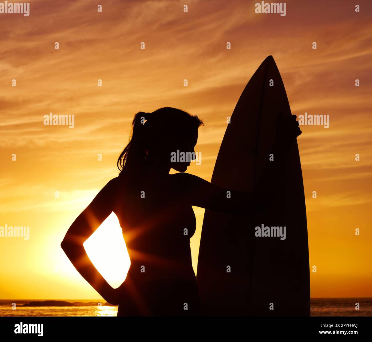 Frau mit Surfbrett vor dem malerischen Sonnenuntergang - Silhouette. Malerischer Blick auf eine Frau mit Surfbrett bei Sonnenuntergang - Silhouette. Stockfoto