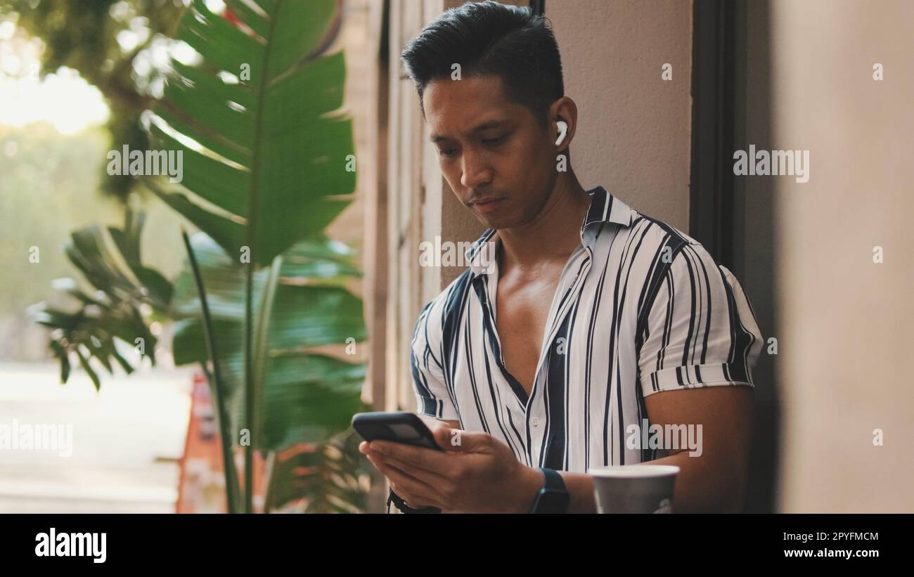 Der junge Mann sitzt draußen und benutzt ein Handy Stockfoto