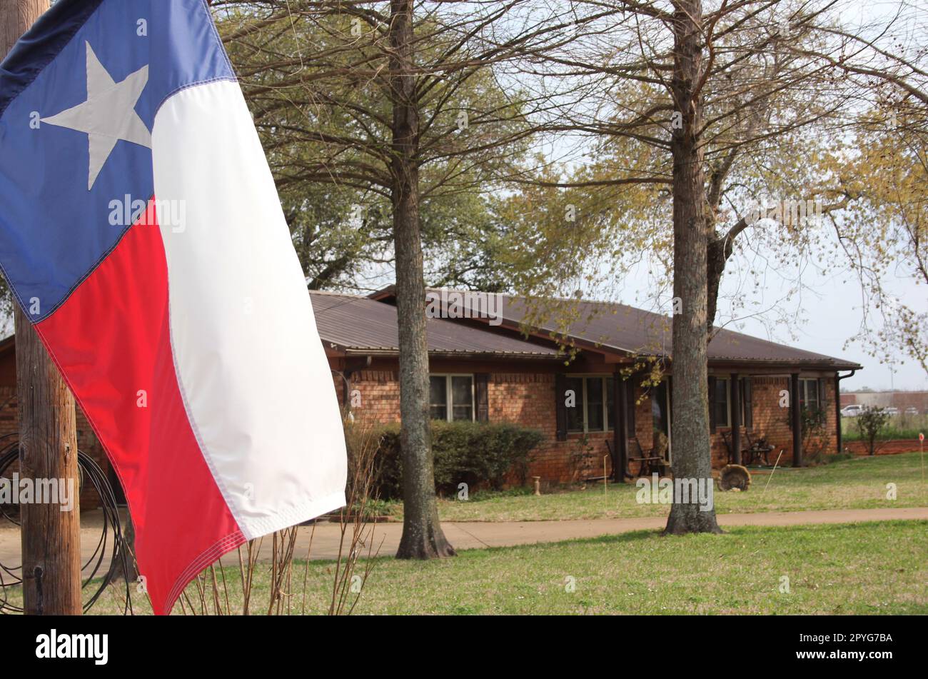 Texas Flag mit Brick Ranch House im Hintergrund Stockfoto