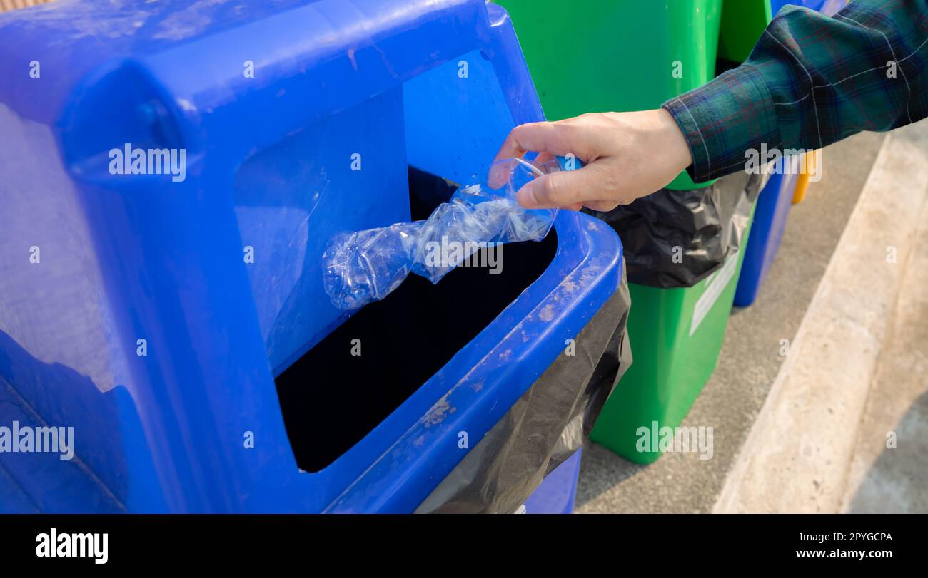 Die Leute werfen leere Wasserflaschen in den Papierkorb. Blauer Kunststoff-Papierkorb. Mann entsorgen Sie die Wasserflasche in den Mülleimer. Abfallbewirtschaftung. Plastikflaschen-Müll. Kunststoffkonzept reduzieren und wiederverwenden. Stockfoto