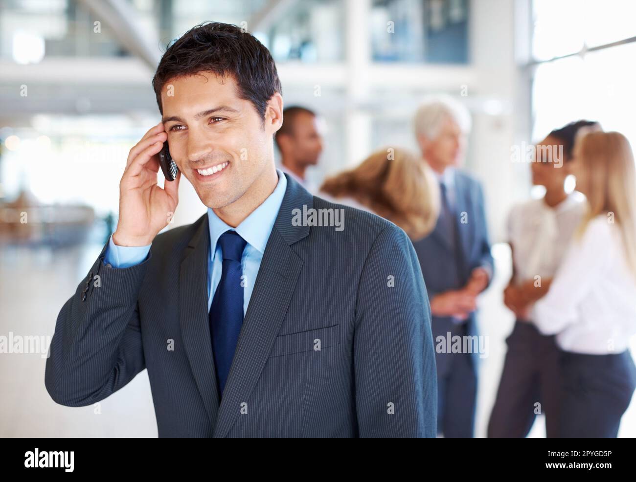 Männliche Führungskraft auf Abruf mit Gruppendiskussion. Porträt eines attraktiven männlichen Bereitschaftsleiters mit Geschäftsleuten, die im Hintergrund diskutieren. Stockfoto