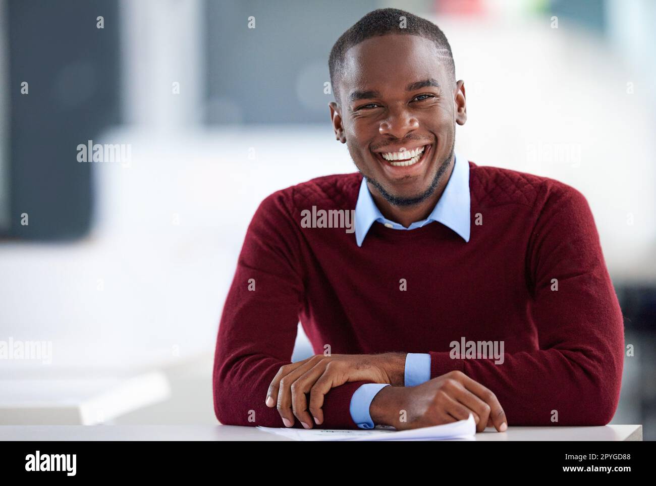 Meine Karriere ist im Trend. Porträt eines lächelnden jungen Geschäftsmannes, der an einem Schreibtisch in einem Büro sitzt. Stockfoto