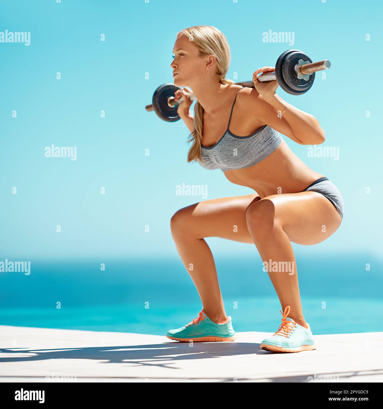 Ihr Körper schreit nach Kraft. Die volle Länge einer attraktiven jungen Frau, die draußen mit einer Barglocke Squats macht. Stockfoto