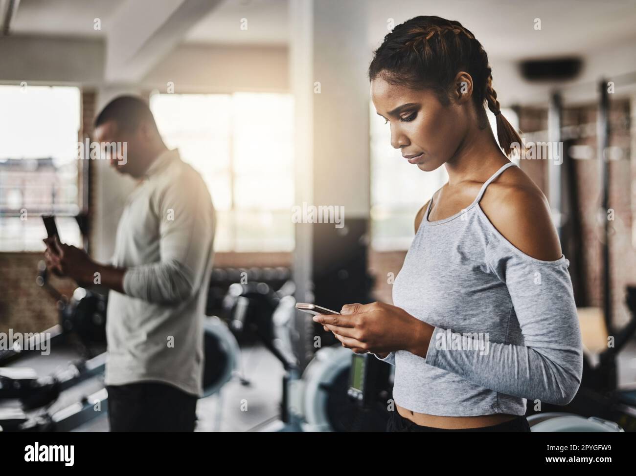 Fitness-Center mit Smart Apps. Eine junge Frau, die ein Handy im Fitnessstudio benutzt. Stockfoto