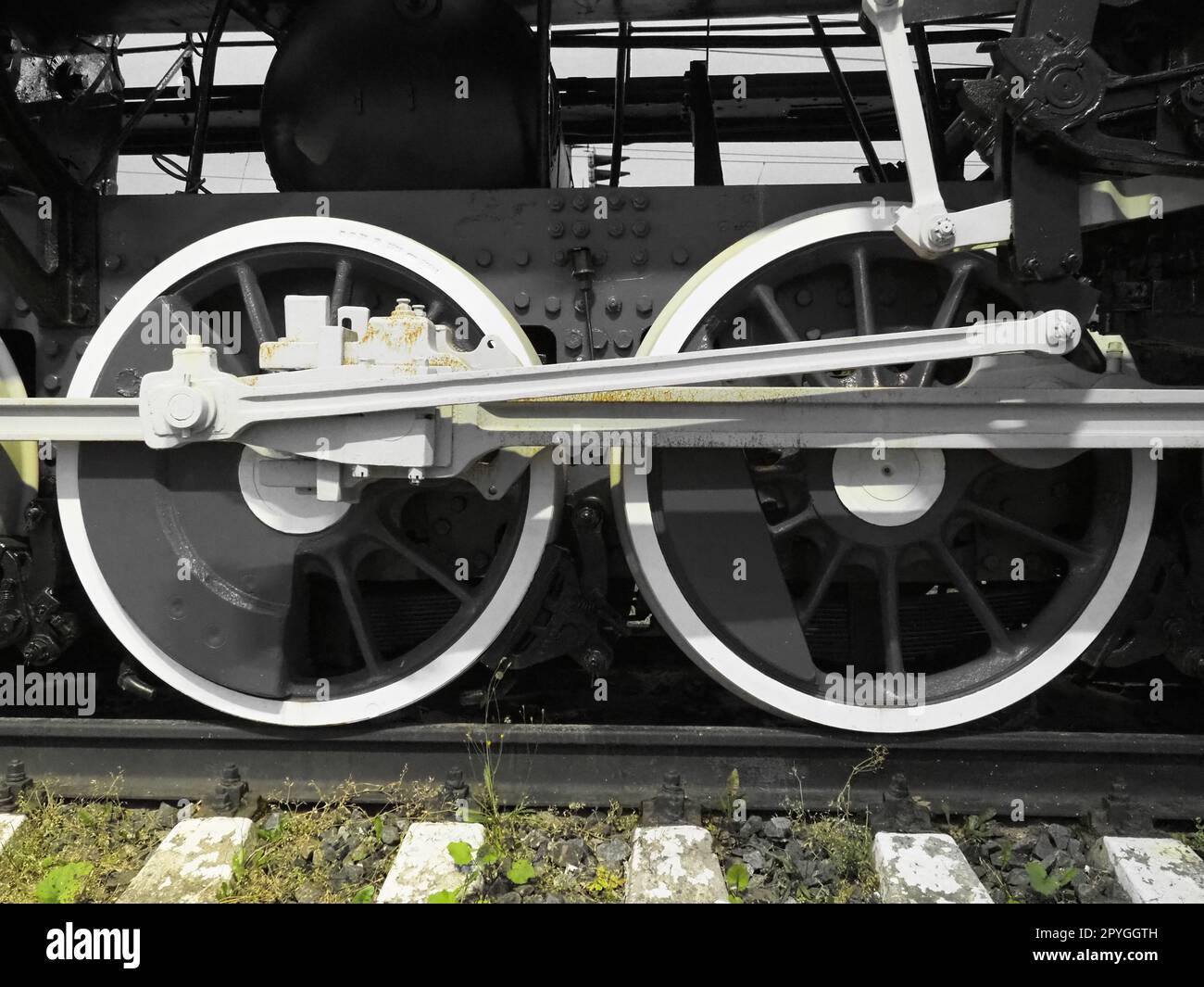 Zwei Räder nachrüsten. Schwellen und Schienen, Mechanismen, Kolben und Führungen. Lokomotive des 19. Frühen 20. Jahrhunderts mit Dampfmaschine. Schwarz-weiße Räder mit grünem Gras. Vintage-Style Stockfoto