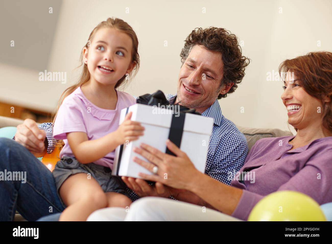 Lassen Sie mich raten, was das ist... eine Familie, die im Wohnzimmer mit einem Geschenk sitzt. Stockfoto