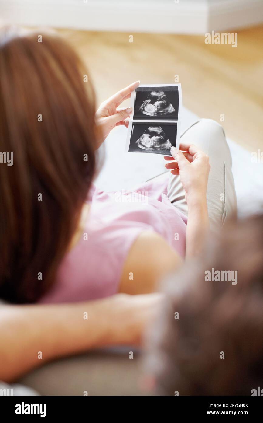 Ich weiß nicht, ob es ein Junge oder ein Mädchen ist. Über die Schulter sehen, wie eine junge schwangere Frau ihr Baby-Sonogramm ansieht. Stockfoto