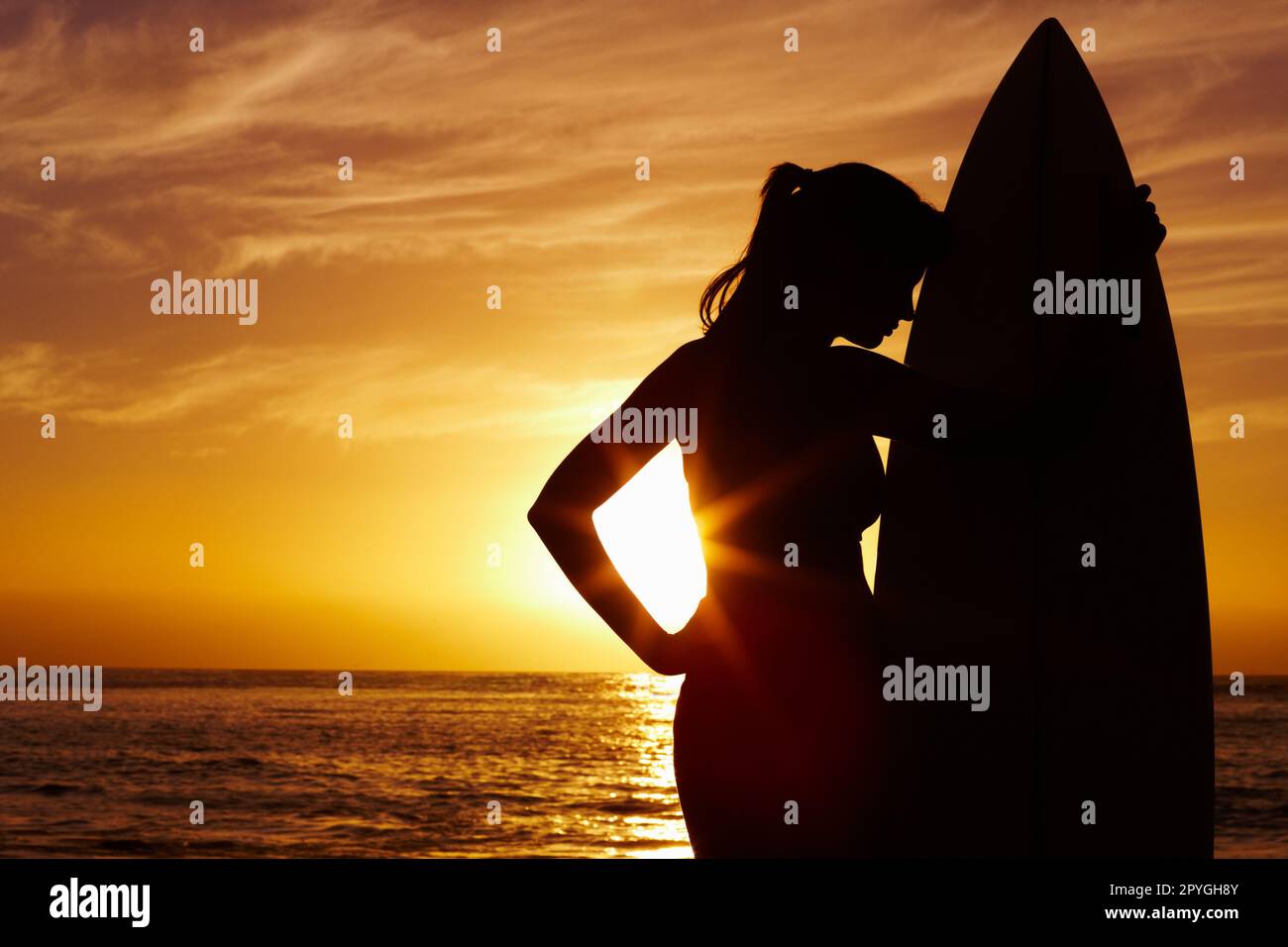 Silhouette Frau mit Surfbrett vor dem malerischen Sonnenuntergang auf dem Meer. Silhouettenbild einer Frau mit Surfbrett vor dem malerischen Sonnenuntergang auf dem Meer. Stockfoto
