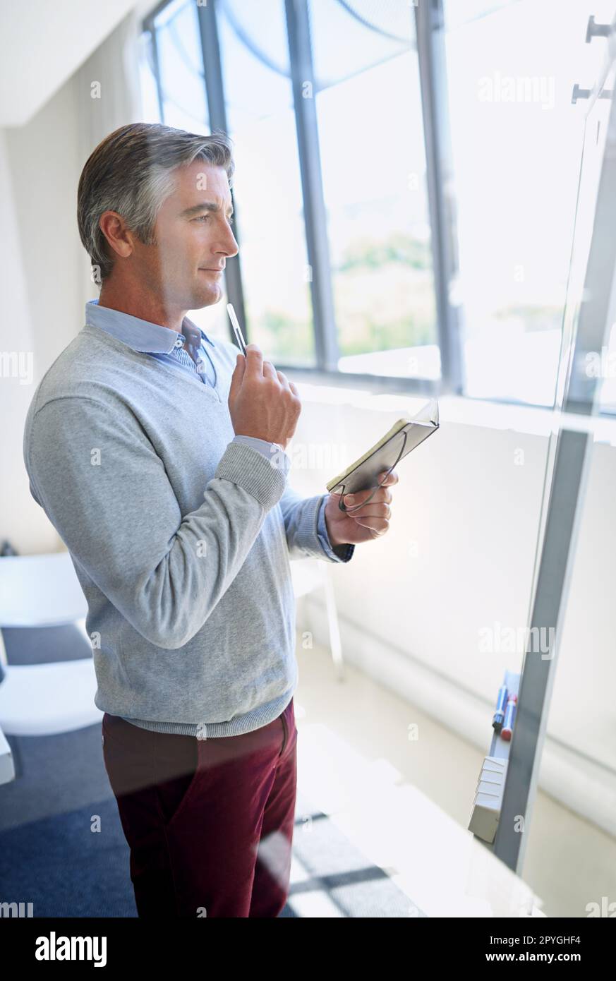 Marketing- und Branding-Lösungen für Sie. Ein reifes Unternehmen, das aufmerksam aussieht, während es an einem Whiteboard mit einem Notebook steht. Stockfoto