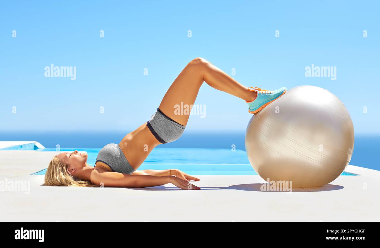 Ganzkörpertonisierung. Eine attraktive junge Frau, die mit einem Sportball am Pool trainiert. Stockfoto