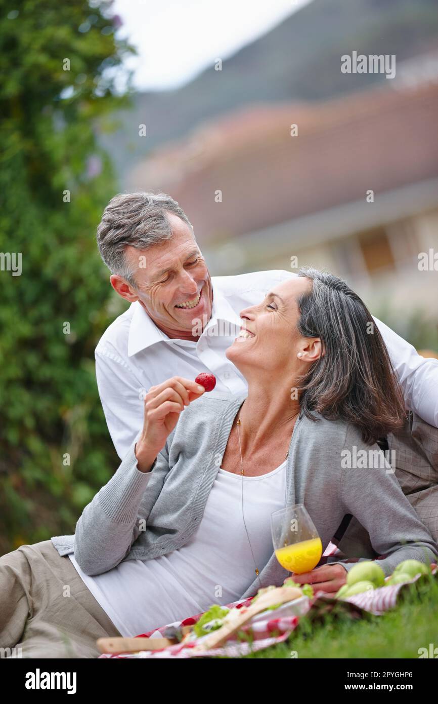 Die Romantik am Leben erhalten. Ein liebevolles, reifes Paar, das ein romantisches Picknick auf dem Rasen macht. Stockfoto