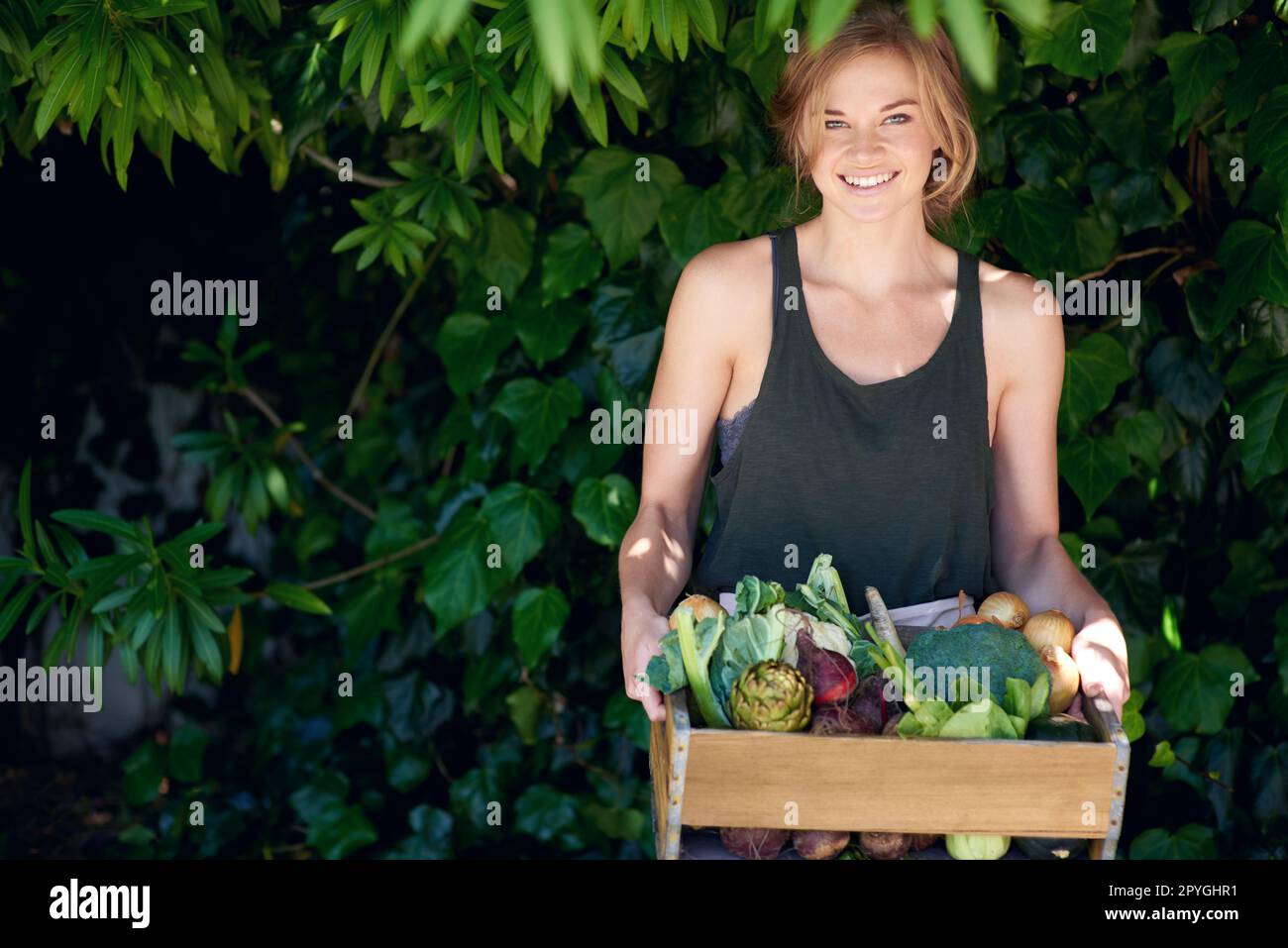 Sparen Sie auf einfache Weise Geld. Eine junge Frau, die eine Kiste Gemüse im Freien hält. Stockfoto