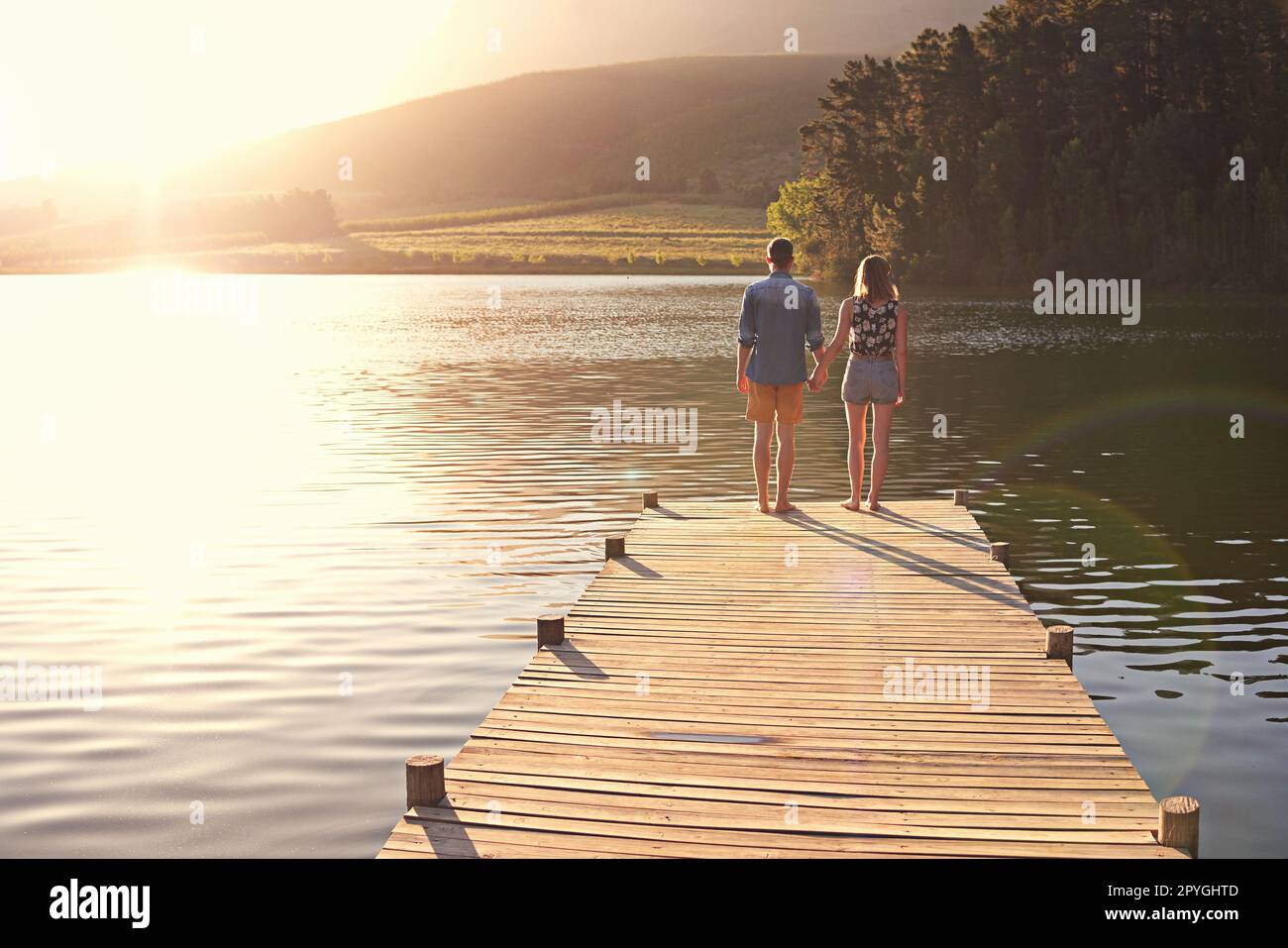 Liebe am See. Rückblick auf ein liebevolles junges Paar, das bei Sonnenuntergang auf einem Dock steht. Stockfoto