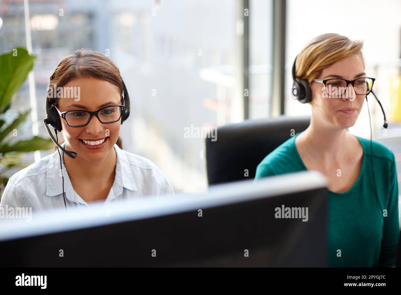 Bereitstellung von Online-Support für ihre Kunden. Zwei weibliche Kundendienstmitarbeiter nehmen Anrufe in ihrem Büro entgegen. Stockfoto