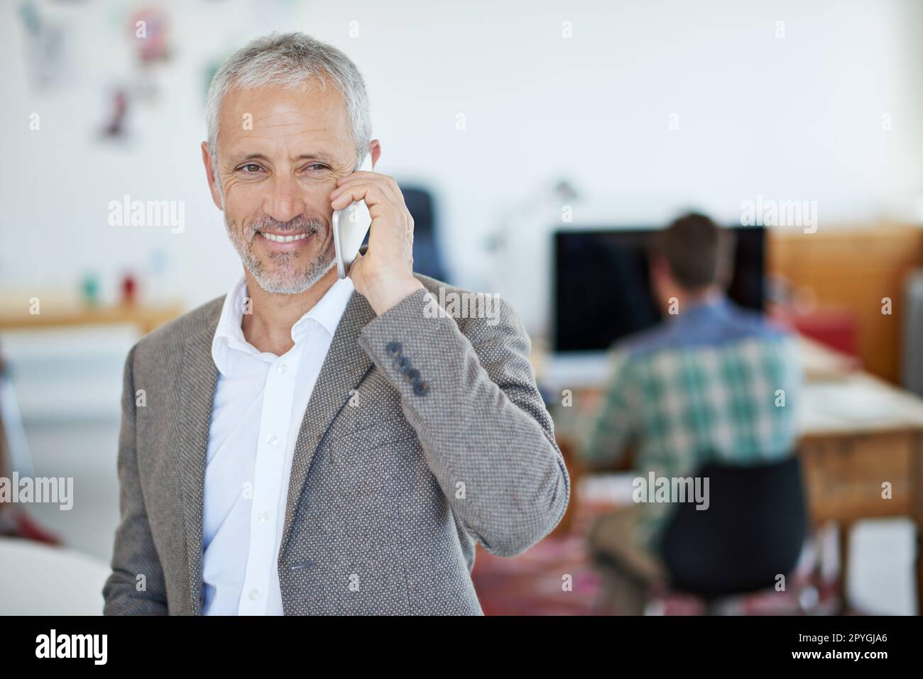 Was kann ich für Sie tun? Porträt eines erwachsenen Geschäftsmannes, der im Büro mit dem Handy spricht. Stockfoto