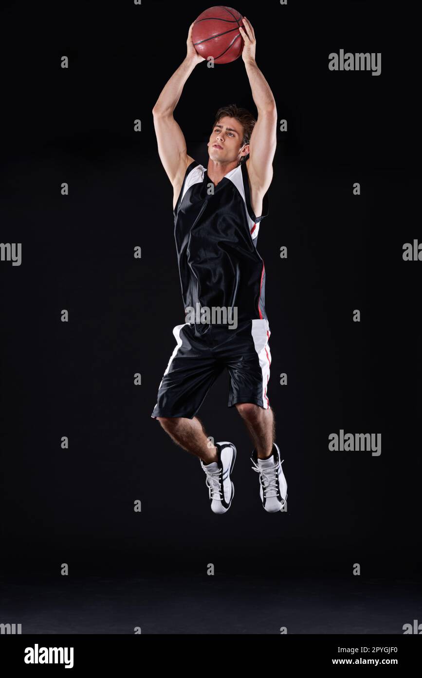 Ich mache einen Slam Dunk. Durchgehende Studioaufnahme eines jungen männlichen Basketballspielers in Aktion vor schwarzem Hintergrund. Stockfoto