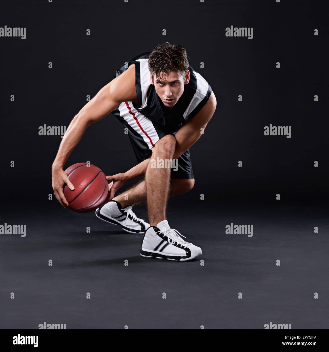 Laufen Sie nicht vor Herausforderungen weg, sondern überfahren Sie sie. Porträt eines männlichen Basketballspielers in Aktion vor schwarzem Hintergrund. Stockfoto
