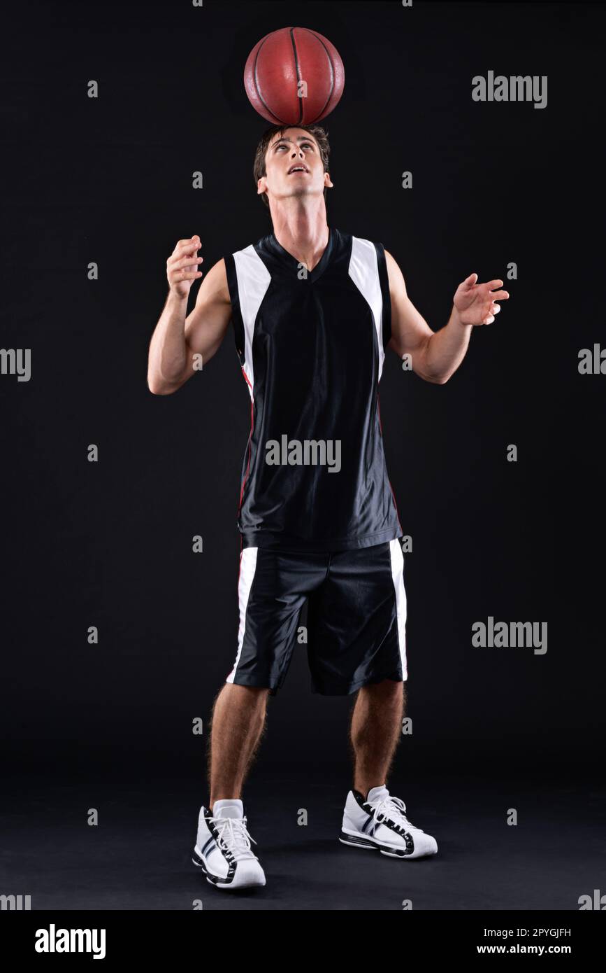 Er zeigt seine Fähigkeiten. Ein männlicher Basketballspieler, der den Ball auf seinem Kopf vor einem schwarzen Hintergrund balanciert. Stockfoto