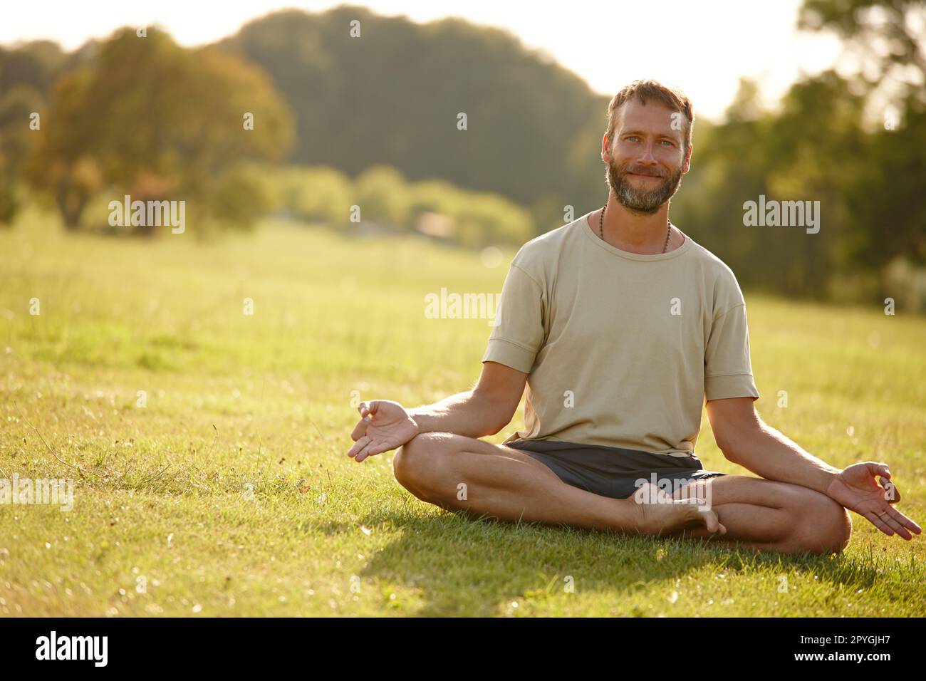Meditieren, wenn die Sonne untergeht. Porträt eines hübschen erwachsenen Mannes, der im Freien Yoga macht. Stockfoto